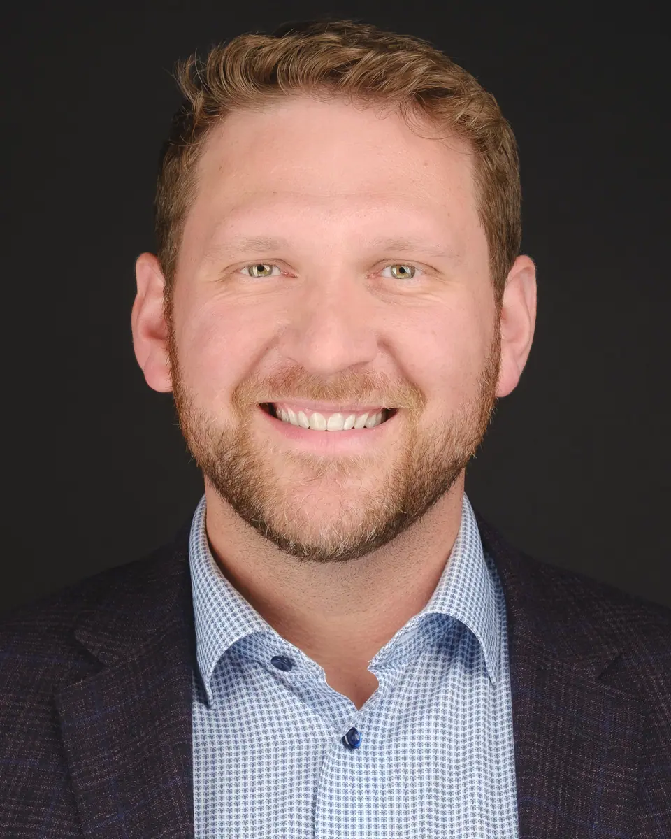 Team headshot of a smiling man with a red beard in a navy blazer