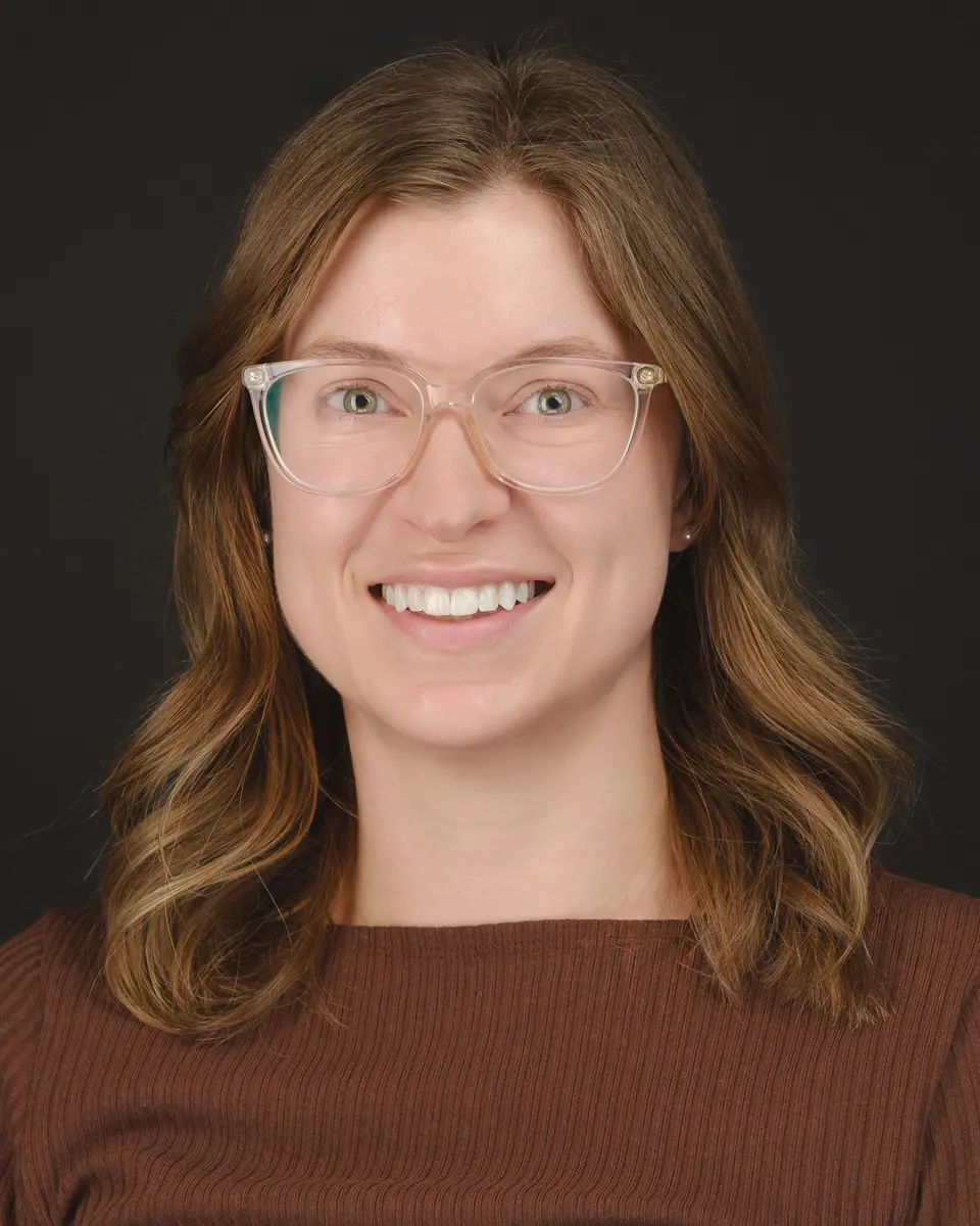 Team headshot of a smiling woman with glasses and wavy hair