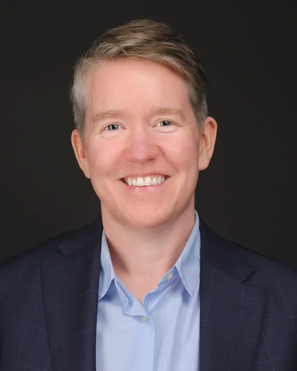 Team headshot of a smiling woman with short hair in a navy blazer and blue shirt