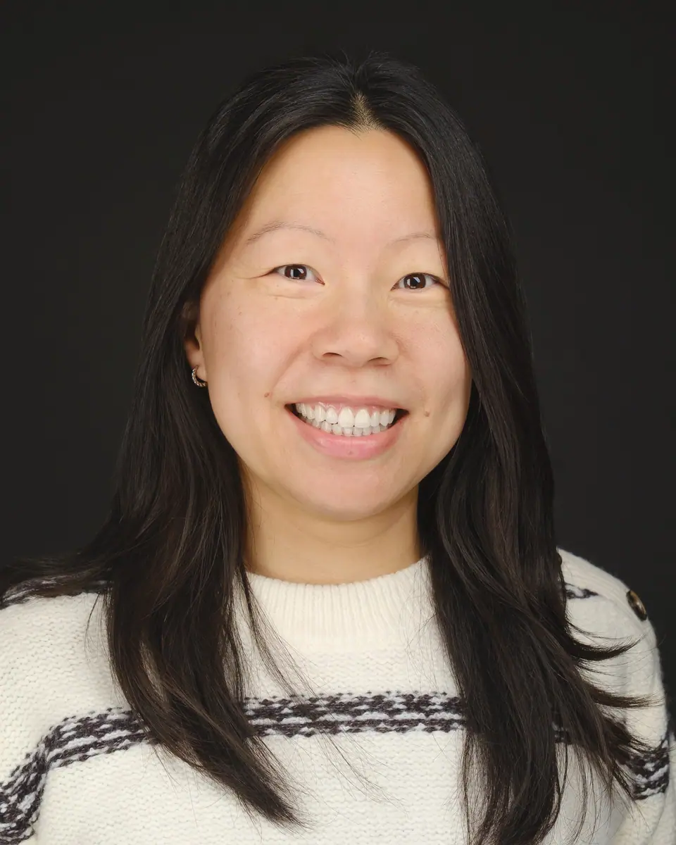Team headshot of a smiling woman with long dark hair in a white sweater